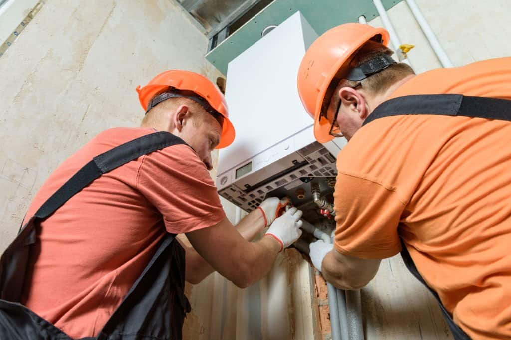workers are connecting the heating system pipes to the gas boiler.